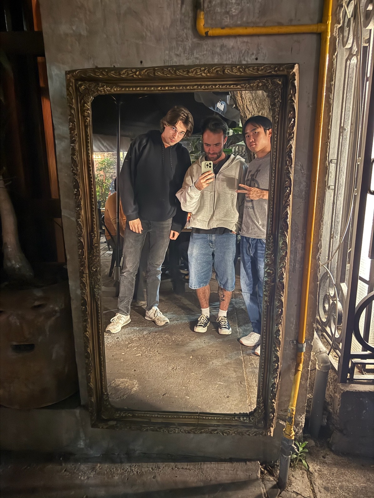 Three teammates taking a selfie in an ornate mirror in a leafy courtyard