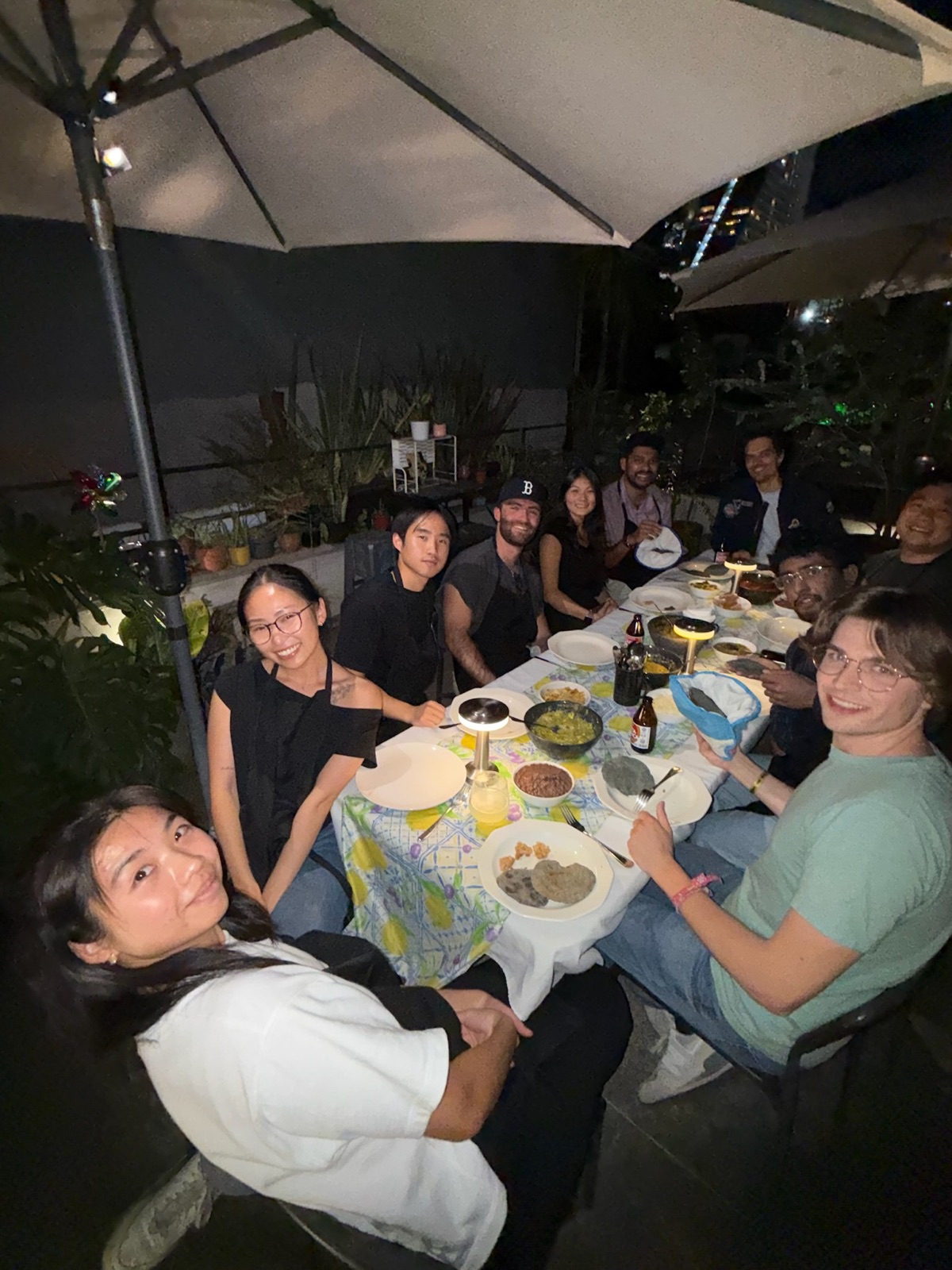 The team around a long rooftop dinner table at night under string lights