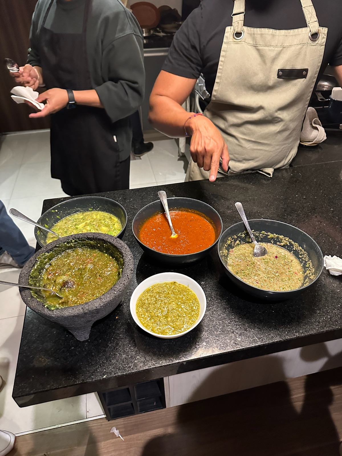 Molcajetes and bowls of freshly made red and green salsas on a kitchen counter
