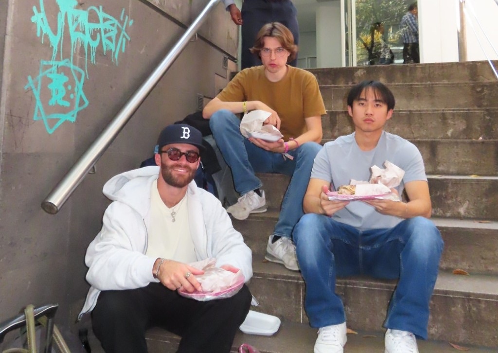 Three teammates eating street food on a set of steps in Mexico City