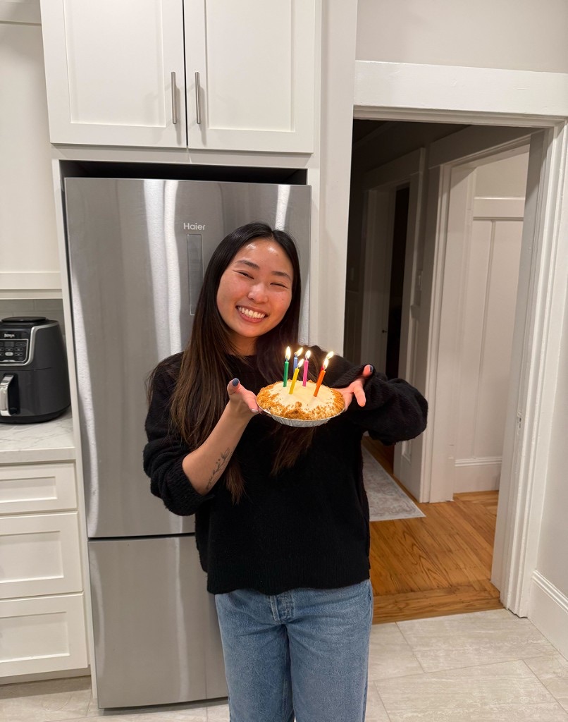 A teammate grinning while holding a pie topped with lit birthday candles in a kitchen