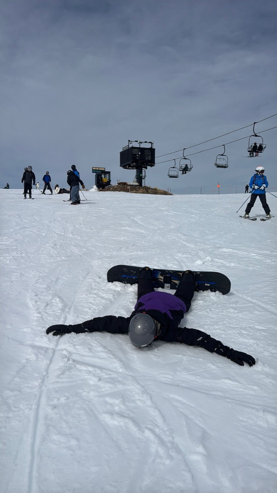 A snowboarder lying spread-eagle in the snow making a snow angel, chairlift behind