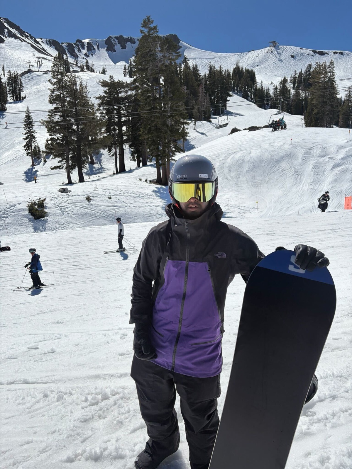 A snowboarder holding their board and posing on a bluebird day in the mountains