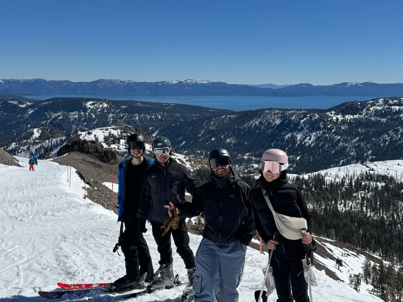 Four teammates in ski gear at a mountain summit with Lake Tahoe far below