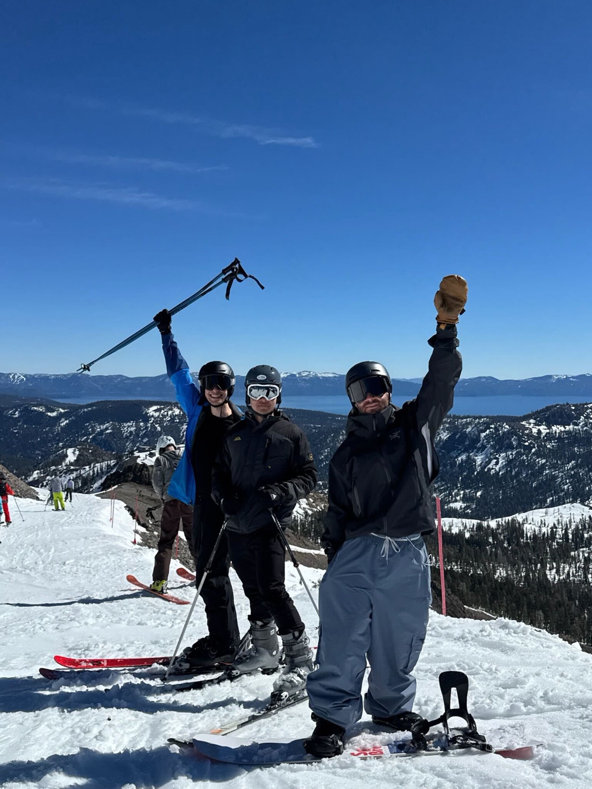 Three teammates raising ski poles in triumph at a mountain summit